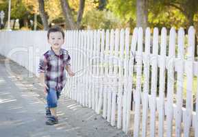 Young Mixed Race Boy Walking with Stick Along White Fence