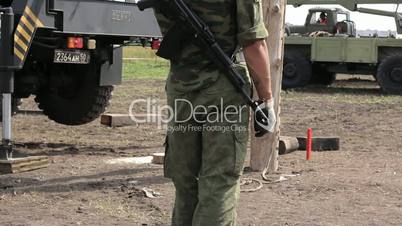 Soldier with ak-47 and working military vehicles in background.