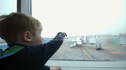 Little boy looking out window and pointing at plane