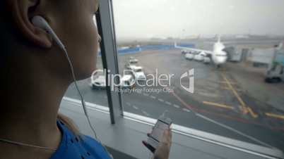 Woman listening to music by the window at airport