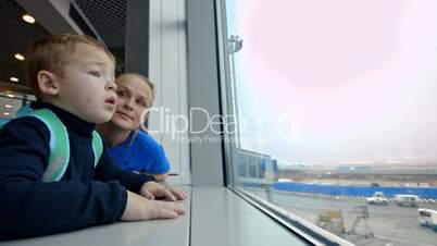 Mother and little son looking out the window at airport