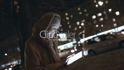 Woman with touch pad typing on her way in night city