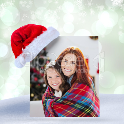 Composite image of festive mother and daughter wrapped in blanke