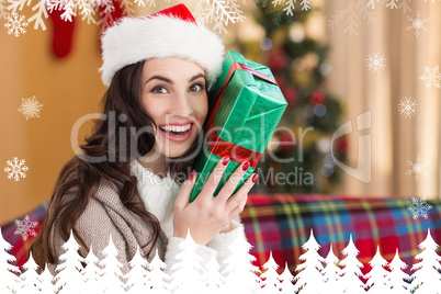 Composite image of festive brunette holding gift at christmas