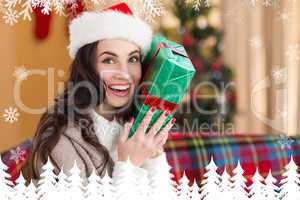 Composite image of festive brunette holding gift at christmas