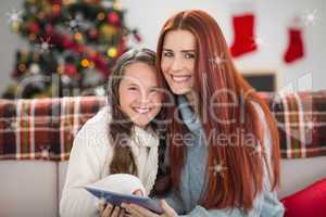 Composite image of festive mother and daughter using tablet on t