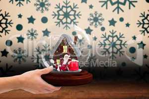 Composite image of hand holding snow globe