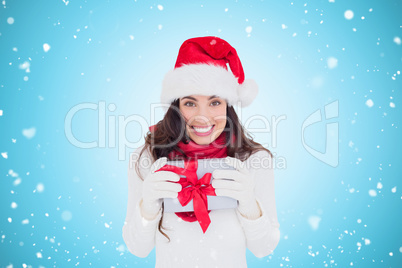 Composite image of festive brunette in santa hat holding gift