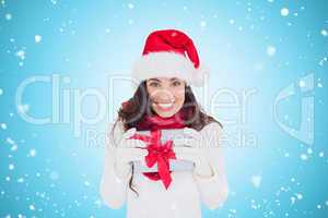 Composite image of festive brunette in santa hat holding gift