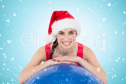 Composite image of festive fit brunette leaning on exercise ball