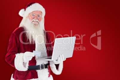 Composite image of santa pays with credit card on a laptop