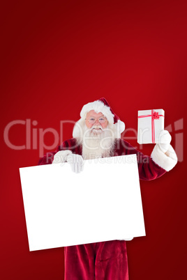 Composite image of santa shows a present while holding sign