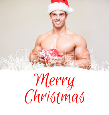 Composite image of shirtless macho man in santa hat holding gift