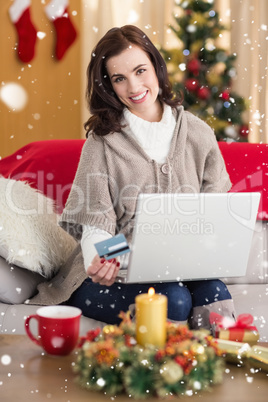 Composite image of smiling brunette shopping online with laptop at christmas