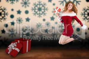 Composite image of festive redhead jumping with gift