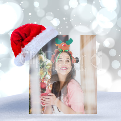 Composite image of smiling brunette in christmas hat holding mug