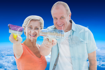 Composite image of happy older couple holding paintbrushes