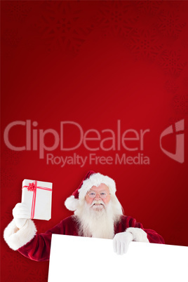 Composite image of santa shows a present while holding sign