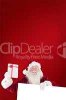 Composite image of santa shows a present while holding sign