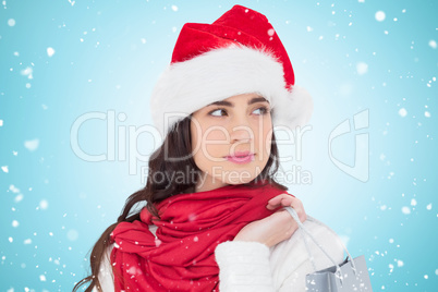 Composite image of brunette in santa hat holding shopping bag