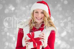 Composite image of smiling young woman in santa hat holding a gi