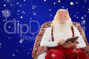 Composite image of smiling santa using tablet on the armchair