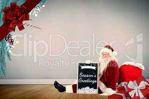 Composite image of santa sits leaned on his bag with a board