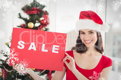 Composite image of festive brunette holding sale sign
