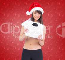 Composite image of festive fit brunette holding a weighing scale