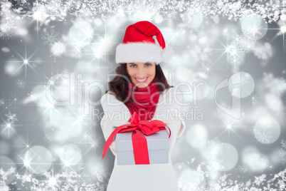 Composite image of festive brunette in santa hat giving gift