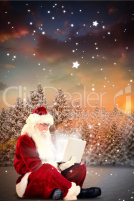 Composite image of santa sits and uses a laptop