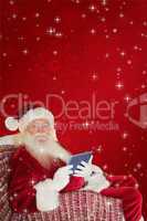 Composite image of smiling santa using tablet on the armchair