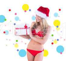 Composite image of festive fit blonde in red bikini showing gift