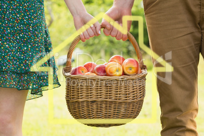 Composite image of basket of apples being carried by a young cou