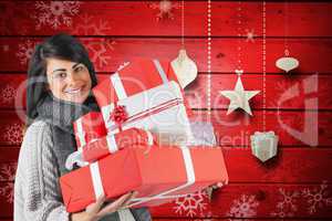 Composite image of smiling brunette holding pile of gifts