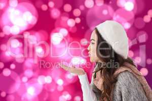 Composite image of brunette in winter clothes blowing kiss
