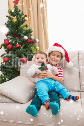 Composite image of cute boy and baby brother on couch at christmas