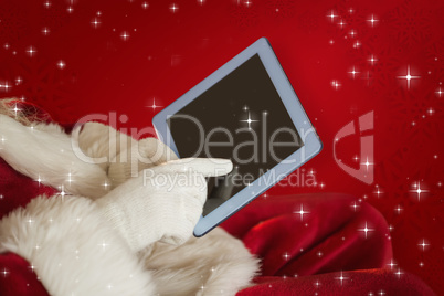 Composite image of santa using tablet on the armchair