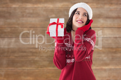 Composite image of surprised brunette in santa hat holding gift