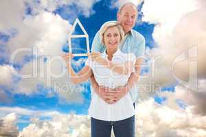 Composite image of happy older couple holding house shape