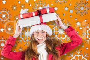 Composite image of festive redhead holding pile of gifts