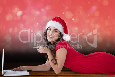 Composite image of festive brunette lying pointing her laptop