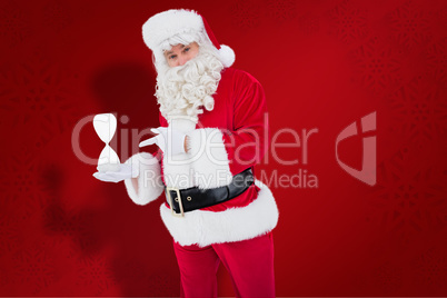 Composite image of smiling santa claus holding hourglass