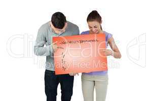 Composite image of young couple pointing at banner they are hold