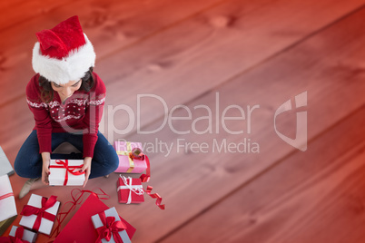 Composite image of festive brunette sitting and wrapping christm