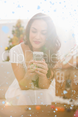 Composite image of beauty brunette using her smartphone on the sofa