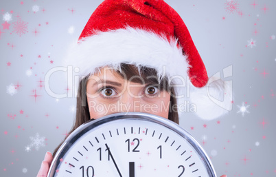 Composite image of portrait of a festive brunette holding a cloc