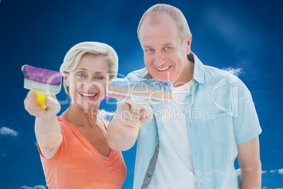 Composite image of happy older couple holding paintbrushes