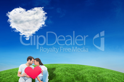 Composite image of cute couple sitting holding red heart