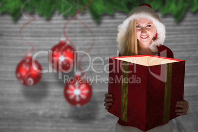 Composite image of festive blonde looking into glowing gift